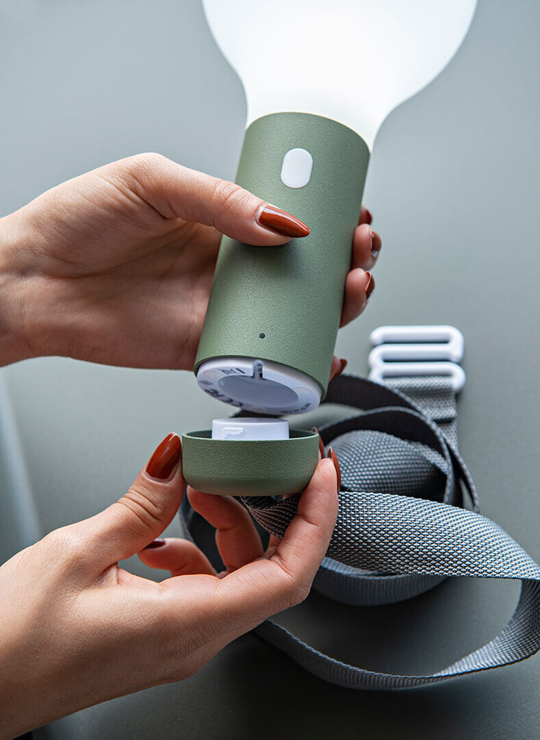 Eine Person hält eine tragbare Lampe mit grünem Magnetsockel »Aplô« in der Hand. Neben der Lampe ist ein graues Band zu sehen.