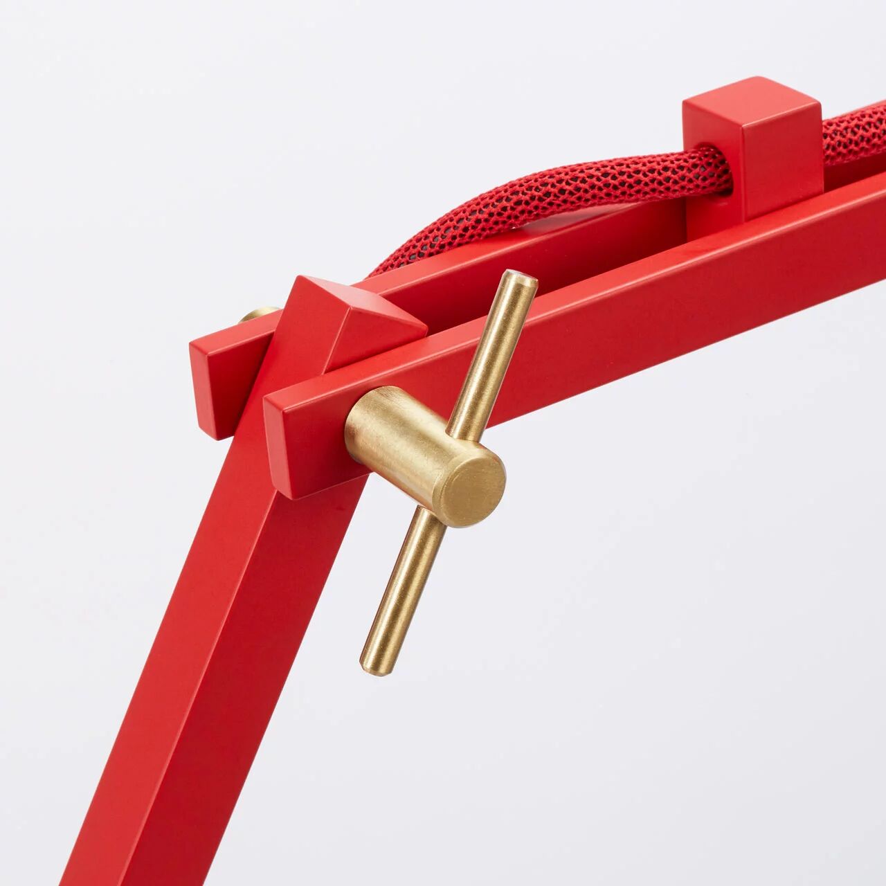 Detailansicht der Stehleuchte »schliephacke« von mawa design: Rotes, kantiges Aluminium-Gestell mit präzisen Kanten, sichtbarem roten Stromkabel mit Textilummantelung und einem messingfarbenen Bedienhebel auf weißem Hintergrund. Hochwertige Materialien treffen auf minimalistische Gestaltung.