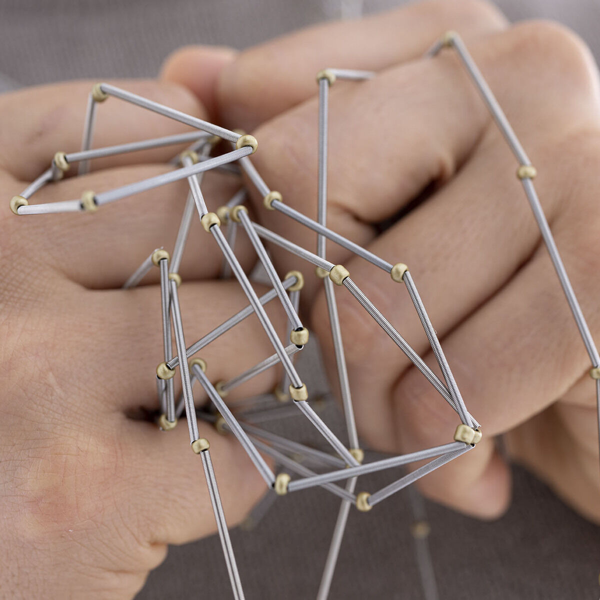 Nahaufnahme einer modernen Kette namens »Rugiada« mit geometrischen Formen in Silber- und Goldtönen, getragen an einer Hand.