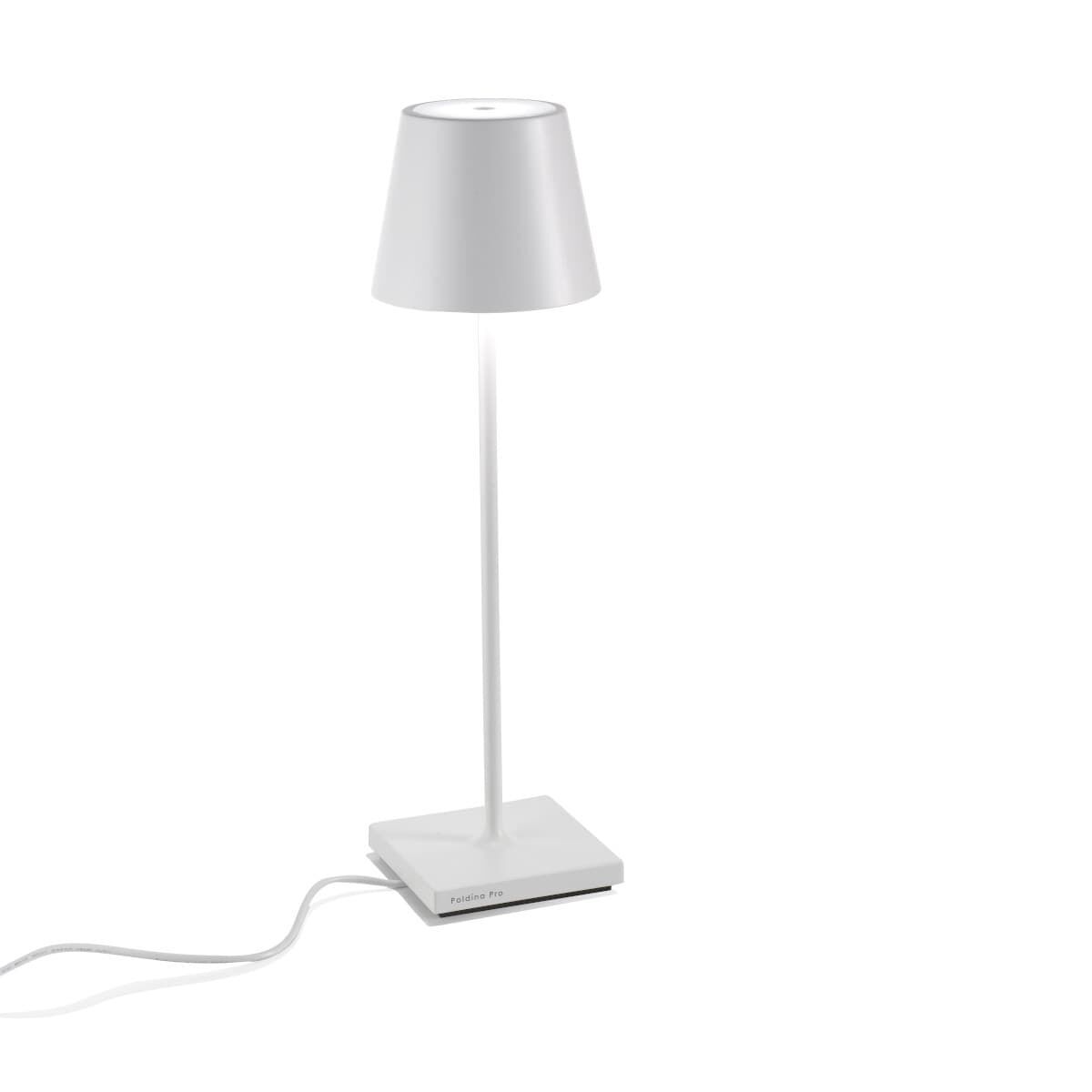 Die LED-Tischlampe »Poldina Pro« hat ein modernes, minimalistisches Design. Sie ist weiß, mit einem silbernen Schalter auf der Basis und hat einen stromlinienförmigen Lampenschirm. Die Lampe ist kabellos und steht auf einer rechteckigen Basis.