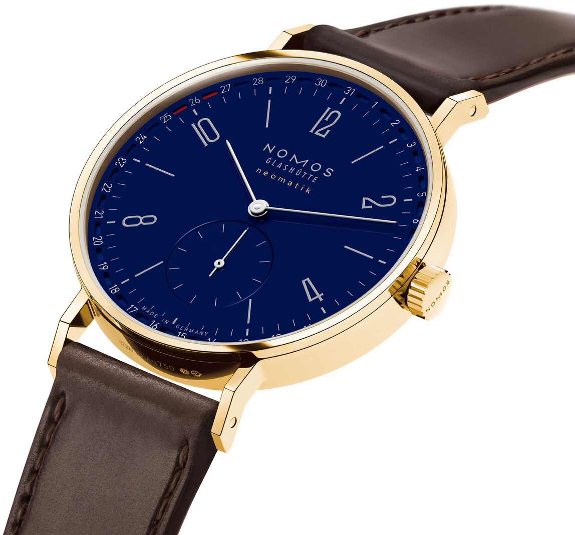 Die ZEITmagazin-Sonderedition Tangente Gold neomatik 38 Update von NOMOS zeigt ein tief emailliertes blaues Zifferblatt, goldenes Gehäuse, feine weiße Indizes, rote Datumsskala und kleine Sekunde. Das edle Armband ist dunkelbraun, das Design wirkt modern und hochwertig.