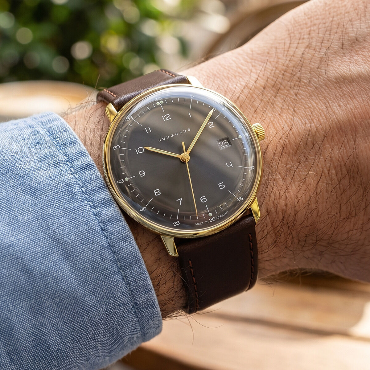 Die ZEIT-Sonderedition Uhr »max bill Quarz« von Junghans mit anthrazit-braunem Zifferblatt, sandgoldfarbenem Edelstahlgehäuse und dunkelbraunem Lederarmband am Handgelenk eines Mannes. Klare Zahlen, Sonnenschliff, goldener Sekundenzeiger, schlankes Bauhaus-Design.