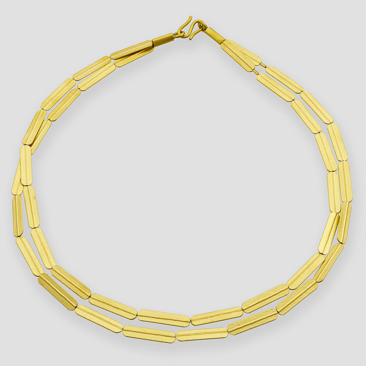 Goldfarbenes und silberfarbenes Collier mit gestreifter, länglicher Gliederstruktur, aus Silber gefertigt und feingoldplattiert. Das moderne Design liegt flach auf grauem Hintergrund und zeigt die hochwertige Verarbeitung des Schmuckstücks, geeignet als elegantes Accessoire für verschiedene Anlässe.