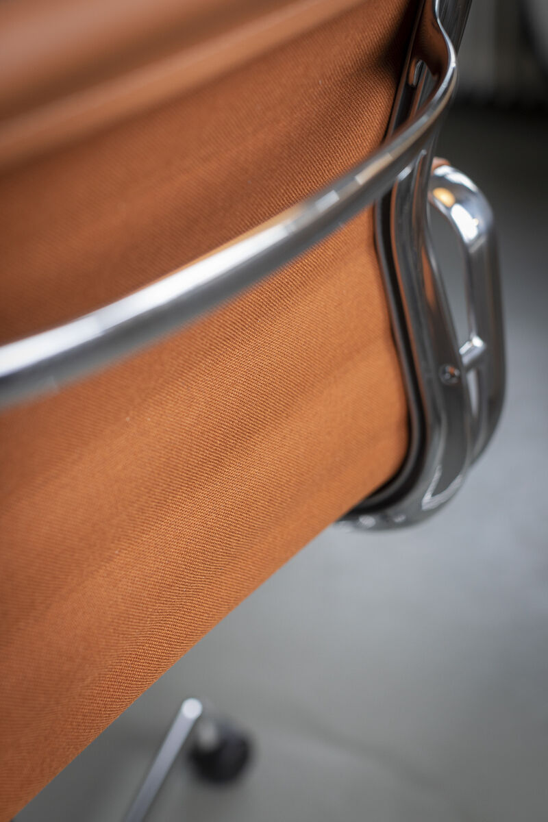 Nahaufnahme eines Vitra Alu Chair EA 118 in Braun, mit einem polierten Metallrahmen und einem Drehmechanismus. Der Stuhl zeigt hochwertige Materialien und ergonomisches Design.