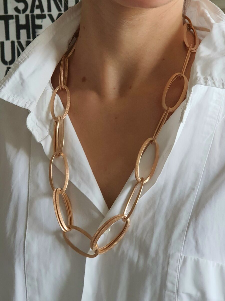 Nahaufnahme einer eleganten goldfarbenen Halskette namens HML-Collier »GRACE«, getragen von einer Person mit weißem Hemd.