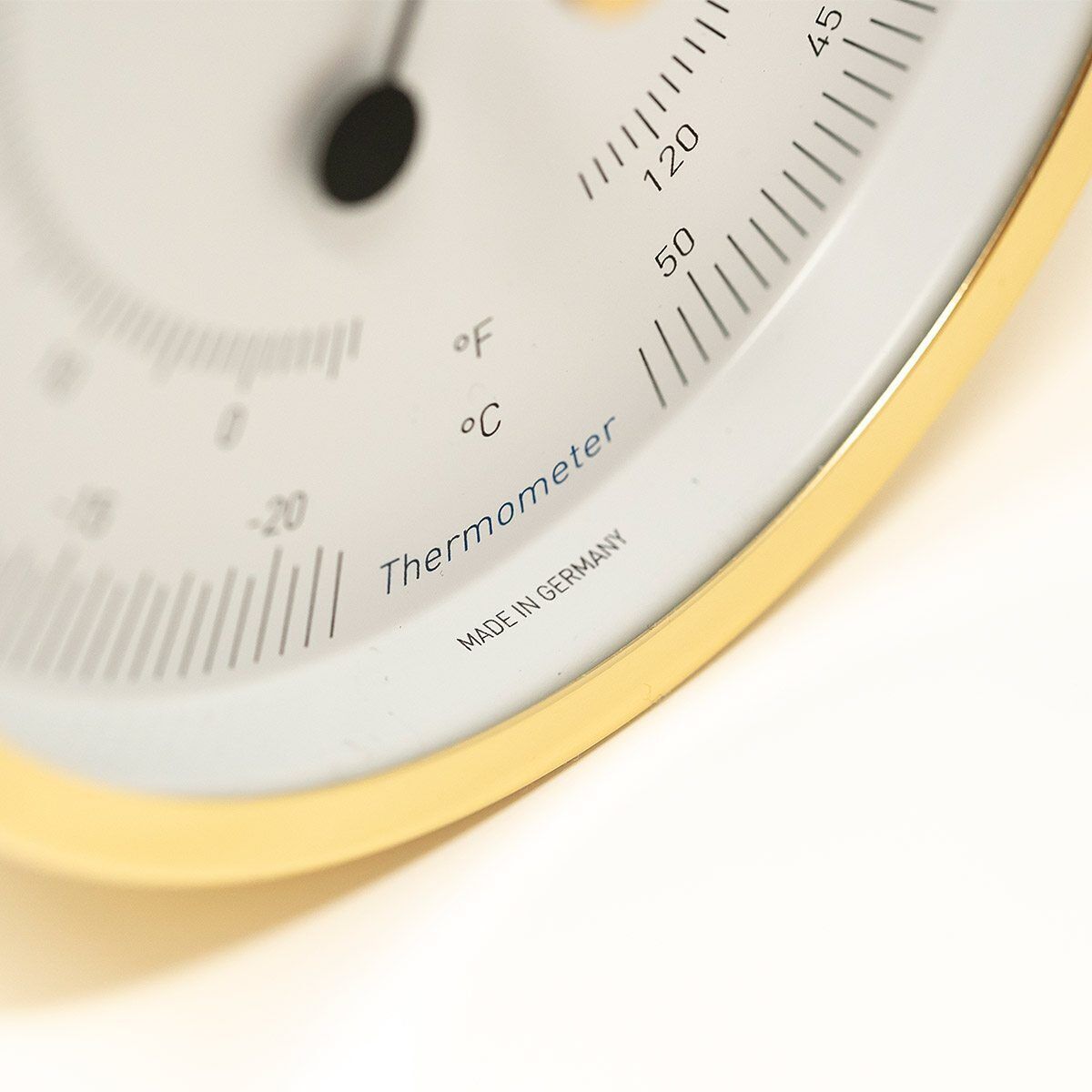 Nahaufnahme eines analogen Thermometers mit weißem Zifferblatt und schwarzen Markierungen sowie einem goldenen Rand. Das Gerät zeigt eine Skala in Grad Celsius und verfügt über eine klare und präzise Anzeige.