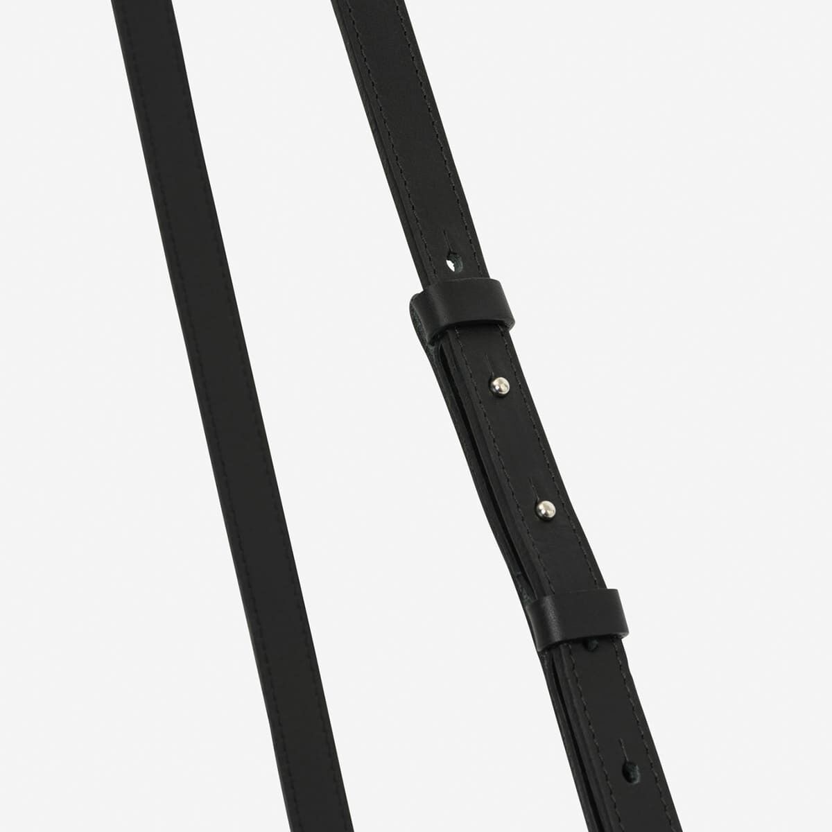 Nahaufnahme eines schwarzen verstellbaren Schulterriemens aus Leder, der Teil einer Tasche ist. Silberne Nieten verleihen dem minimalistischen Design Eleganz.