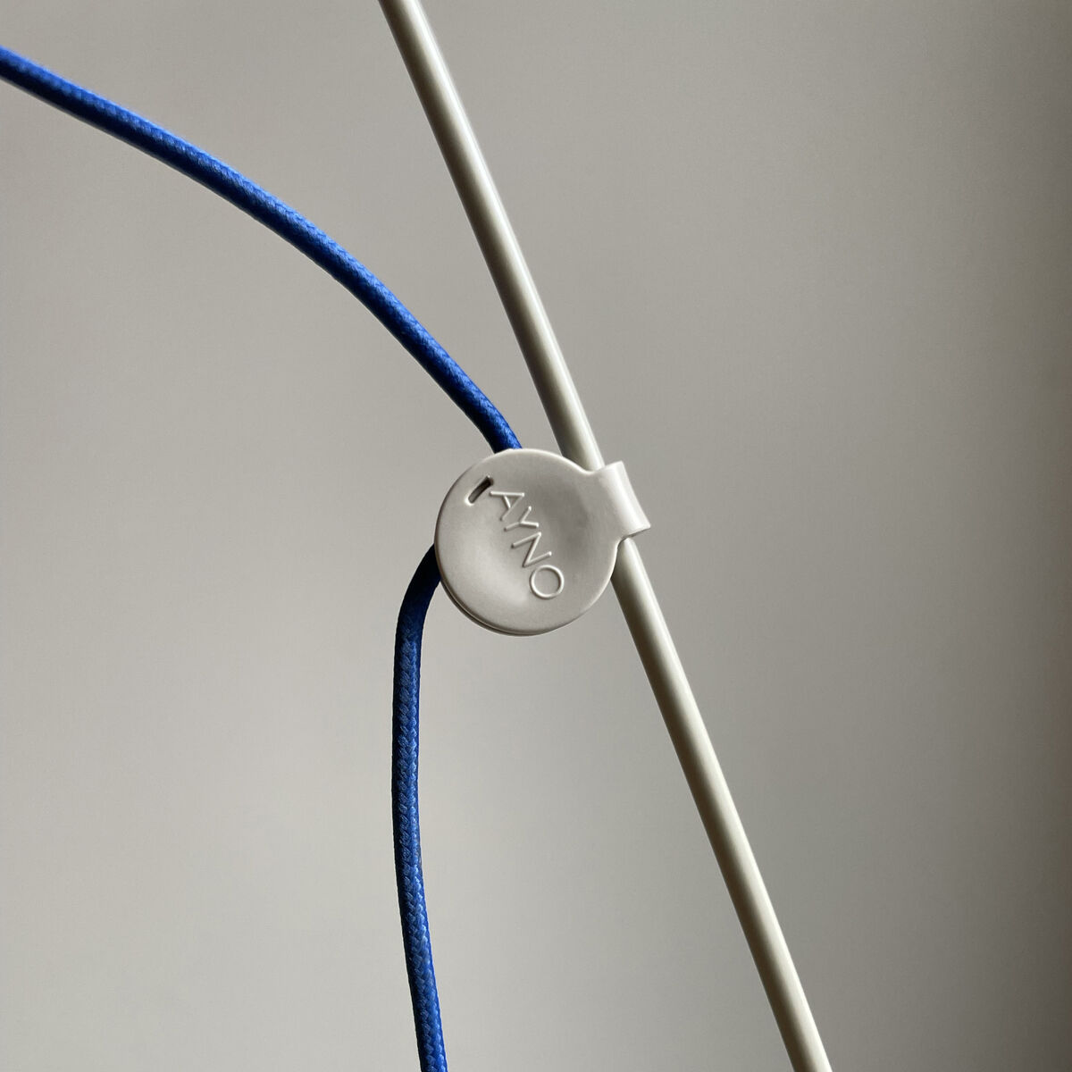 Detailansicht der ZEIT-Sonderedition Stehlampe AYNO in Silk und Ultramarin mit flexiblem blauen Kabel und filigranem silbergrauen Rahmen vor neutralem Hintergrund.