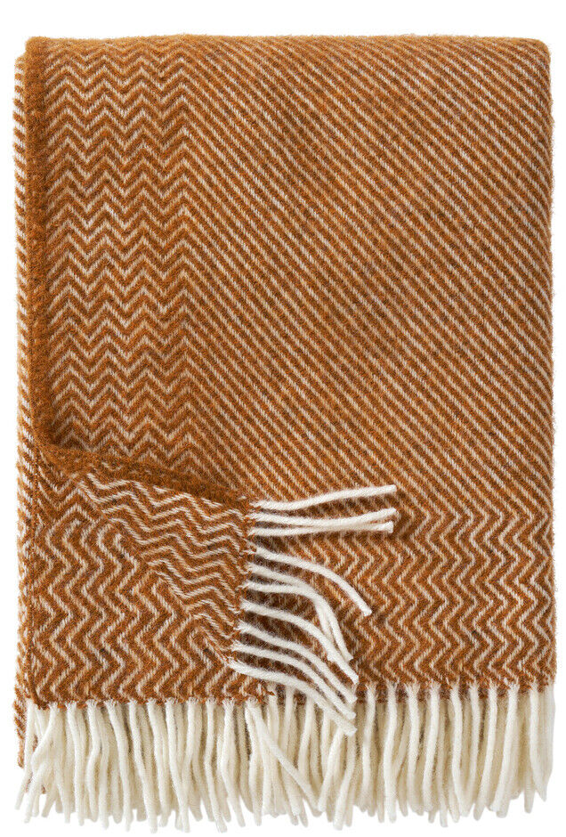 Eine Decke in orange mit weißen Fransen und einem strukturierten Zickzack-Muster. Ideal für den Innenbereich zur Dekoration oder zum Kuscheln.