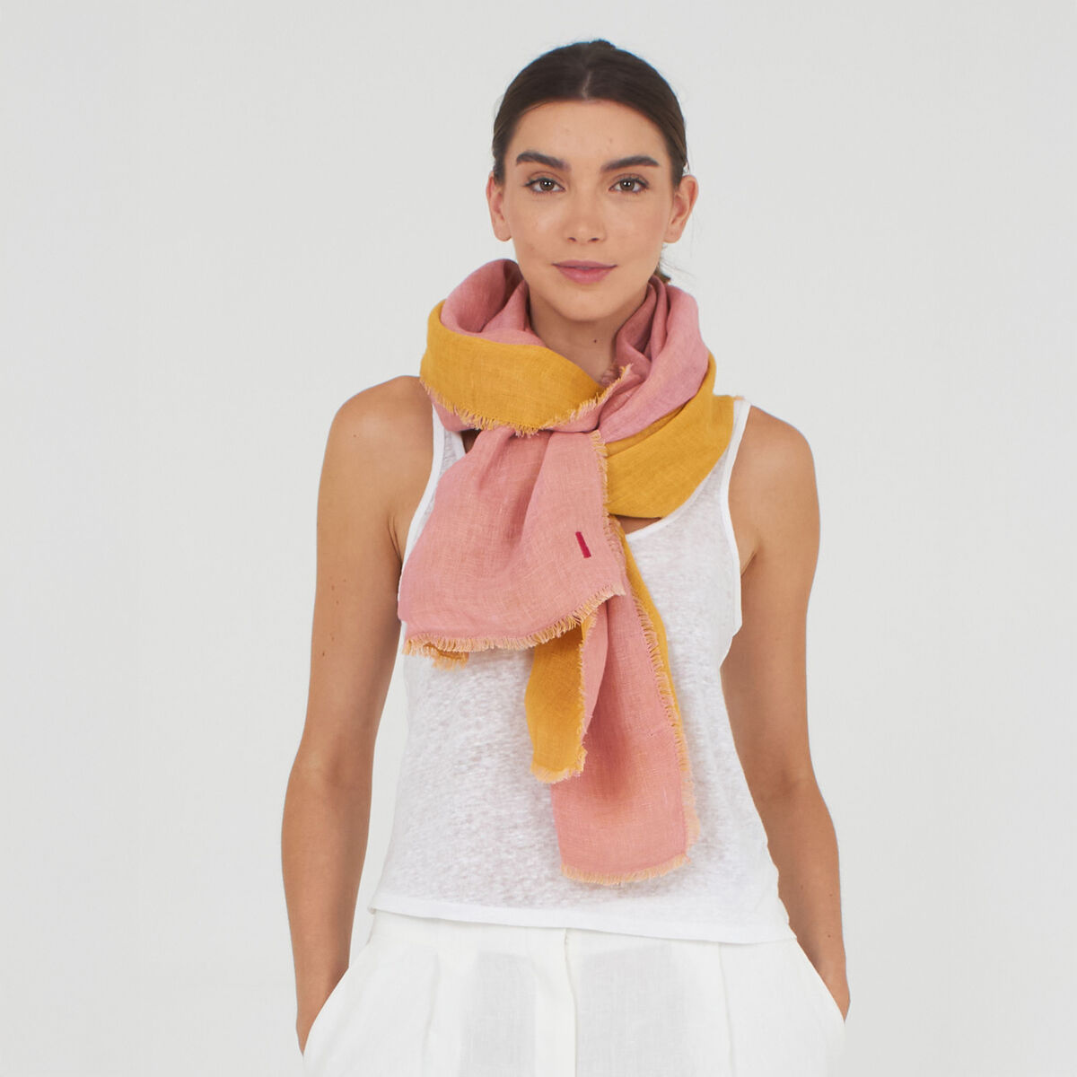Eine Frau trägt einen auffälligen, zweifarbigen Leinenschal »Alsi« von Shalls Barcelona in Pink und Gelb um den Hals. Sie trägt ein weißes ärmelloses Oberteil, darunter scheint ein feines Muster durch. Der Schal ist voluminös und wirkt angenehm weich und stylisch.