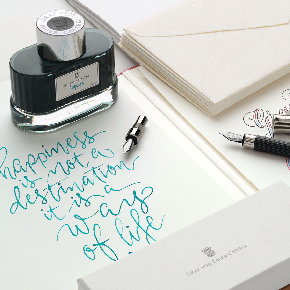 Das Bild zeigt ein elegantes Kalligraphie-Set Tamitio von Faber-Castell, bestehend aus zwei schwarzen Schreibgeräten mit silbernen Akzenten, einem Tintenfass, zwei Ersatzfedern, edlem Briefpapier mit kalligraphischem Schriftzug und einem weißen Marken-Etui auf einem hellen Untergrund. Das Set eignet sich ideal für das Schreiben von Einladungen oder persönlichen Briefen.