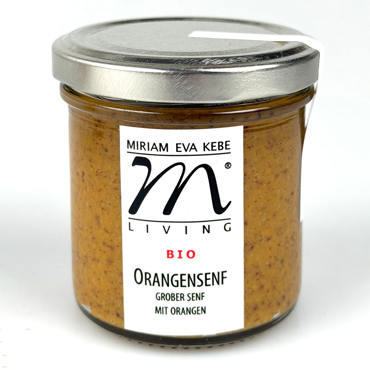 Das Bild zeigt ein rundes Glas mit silbernem Metalldeckel, gefüllt mit orangefarbenem Bio-Orangensenf. Auf dem Glas ist ein weißes Etikett mit schwarzem Schriftzug: 'Miriam Eva Kebe', 'Living', 'BIO', 'Orangensenf grober Senf mit Orangen' zu sehen.