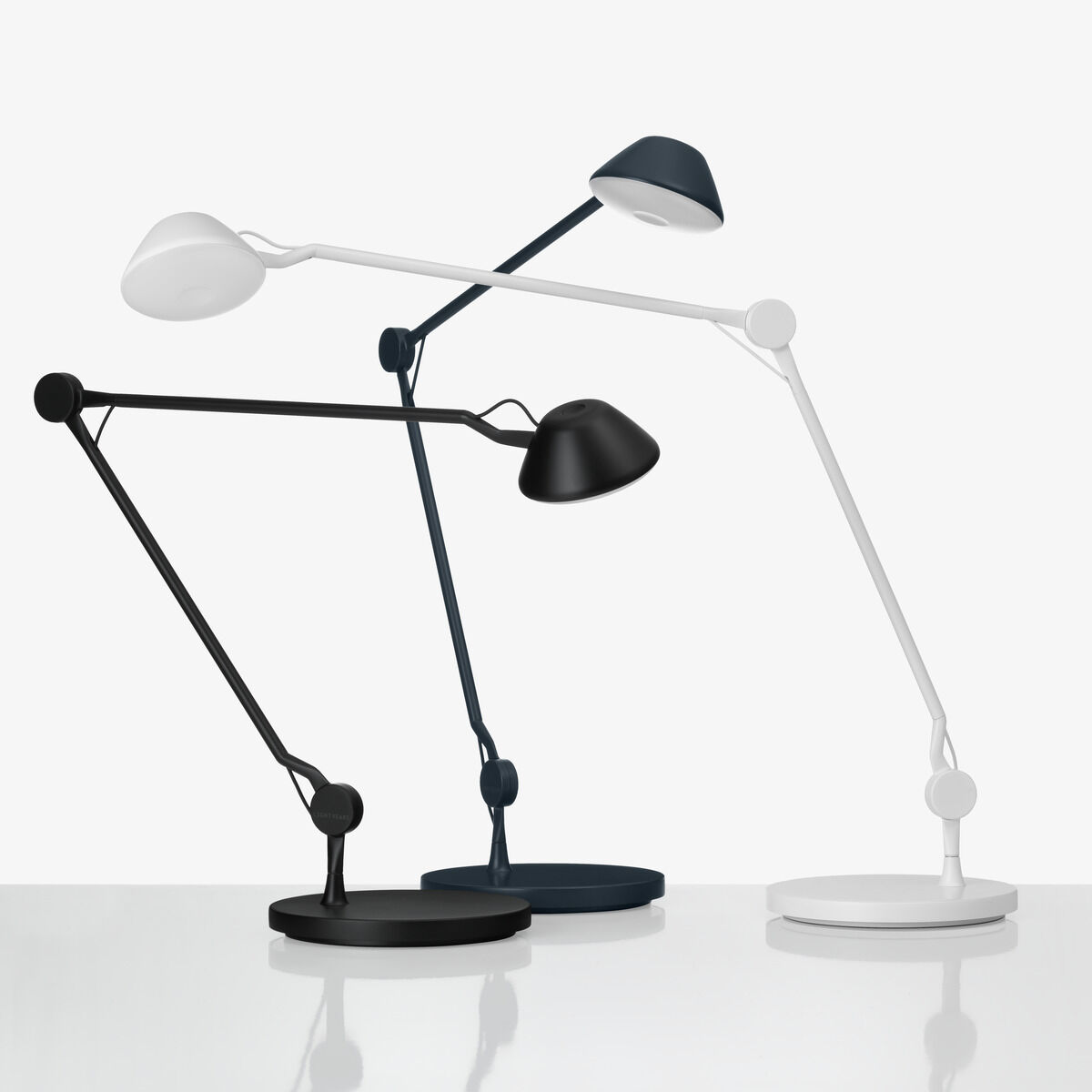 Drei Tischlampen vom Modell AQ01™ von Fritz Hansen in den Farben Schwarz, Weiß und Dunkelblau, auf einem weißen Hintergrund. Die Lampen haben ein minimalistisches, modernes Design und sind verstellbar.