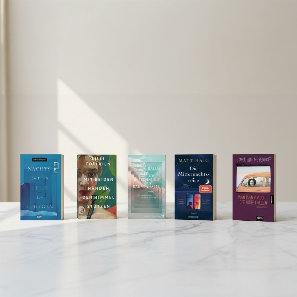 Link zur Kategorie Buchtipps des Monats: Fünf verschiedenfarbige Bücher stehen nebeneinander auf einer weißen Marmorfläche. Die Titel, unter anderem "Nachts ist es leise in Teheran" von Shida Bazyar und "Die Mitternachtsbibliothek" von Matt Haig, sind deutlich zu erkennen. Heller, neutraler Hintergrund.