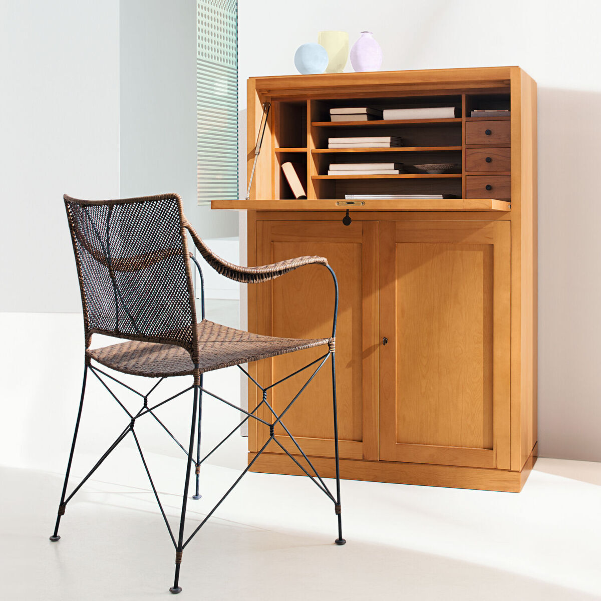 Der ZEIT-Sekretär von MARKTEX (Sonderedition) ist ein vielseitiges Möbelstück aus Holz mit mehreren Fächern und Schubladen für die Organisation. Es steht in einem hellen Raum neben einem schwarzen Metallstuhl mit geflochtener Sitzfläche.
