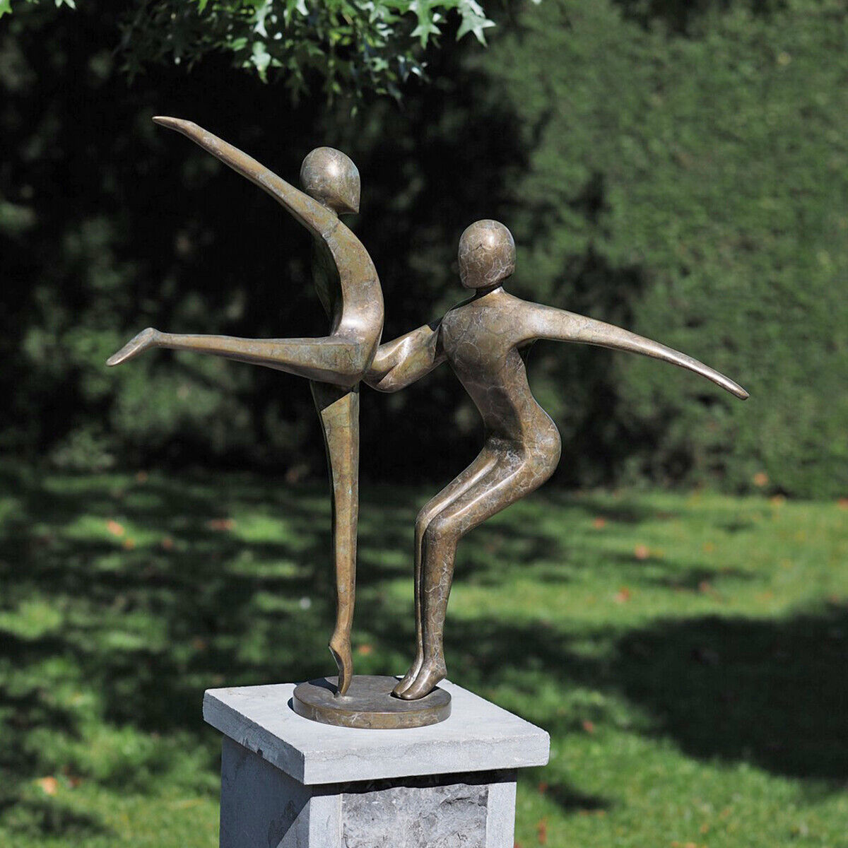 Bronzeskulptur zweier tanzender Figuren auf einem Sockel im Garten. Die Figuren zeigen dynamische Bewegungen und stehen in einem harmonischen Verhältnis zueinander. Im Hintergrund ist grüne Vegetation sichtbar.