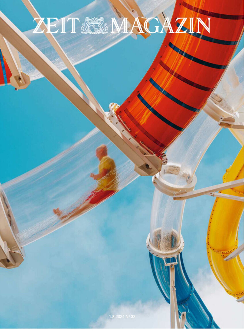 Das Cover des ZEIT Magazins Ausgabe 33/2024 zeigt eine Person, die eine große, durchsichtige Wasserrutsche hinuntergleitet. Der Hintergrund besteht aus einem klaren, blauen Himmel, und die Wasserrutsche hat verschiedene bunte Elemente in Gelb, Rot und Blau.