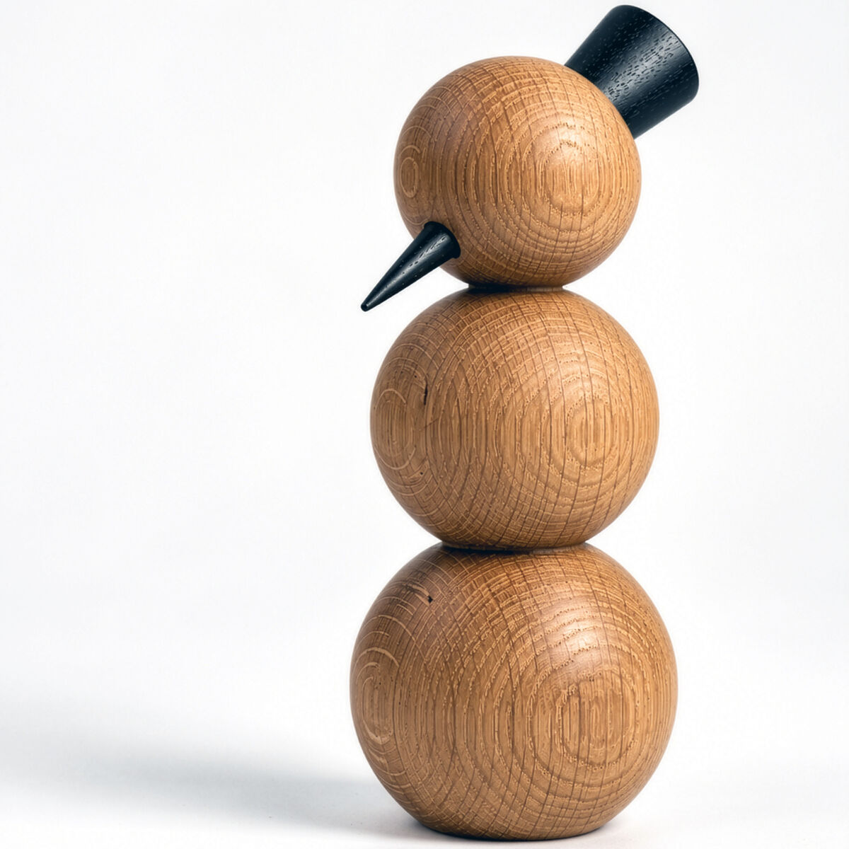 Minimalistische Holzfigur »CLEAR« von finbeaux: Ein Schneemann aus drei übereinandergestapelten, gedrechselten Kugeln aus warm brauner Esche. Der Kopf trägt einen schwarzen, leicht schrägen Zylinder und eine kurze schwarze Kegelnase. Sichtbare Jahresringe prägen das Holz; weißer Studiohintergrund.