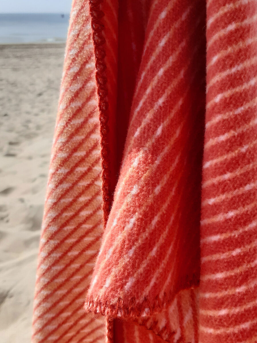 Ein diagonales gestreifte Baumwolldecke in rot und weiß hängt über ein Geländer am Strand.