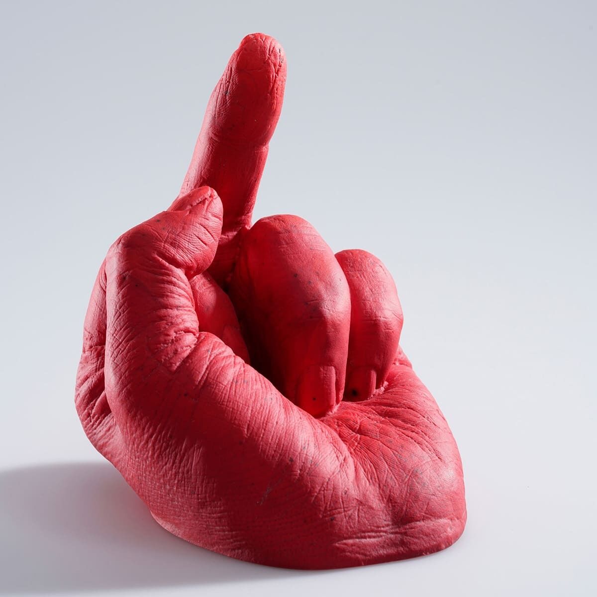 Eine rote Skulptur einer Hand mit ausgestrecktem Mittelfinger, geschaffen von Ai Weiwei, mit dem Titel »Study of Perspective in Glass«. Die Hand zeigt nach oben und ist plastisch gestaltet vor einem grauweißen Hintergrund.