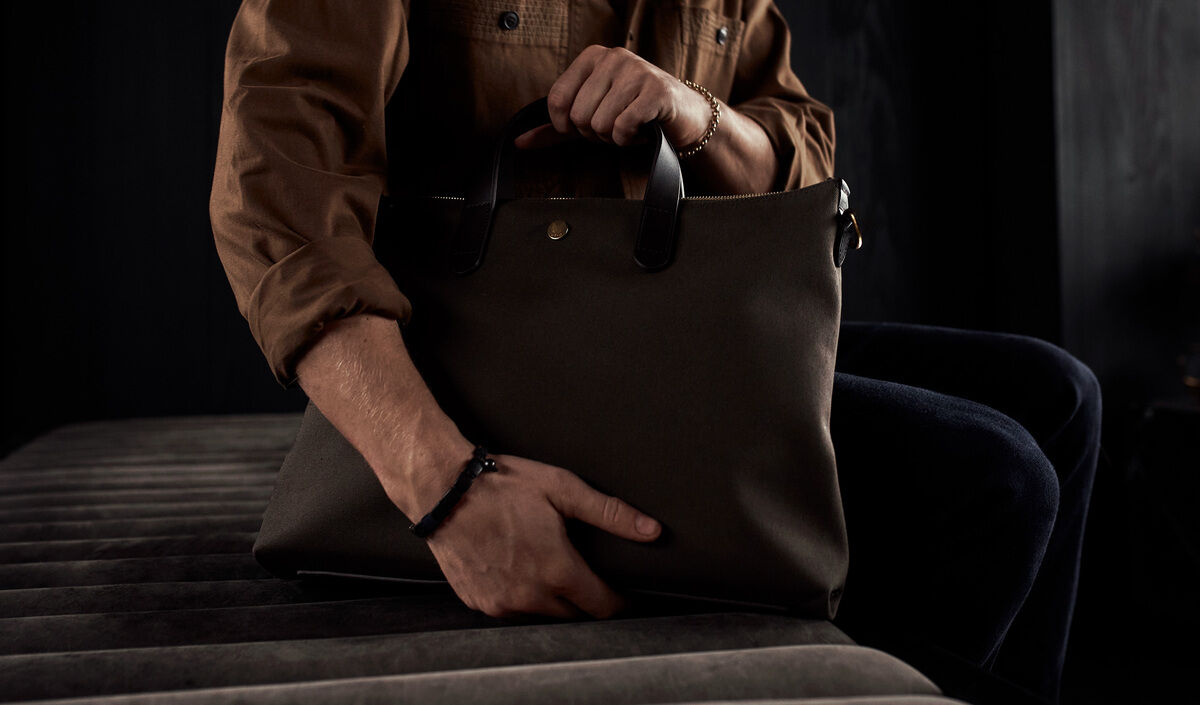 Person hält eine stilvolle, schwarze Laptop-Tasche mit Ledergriffen in der Hand, die aus hochwertigem Material gefertigt ist. Perfekt für Business-Anlässe und den täglichen Berufsalltag.