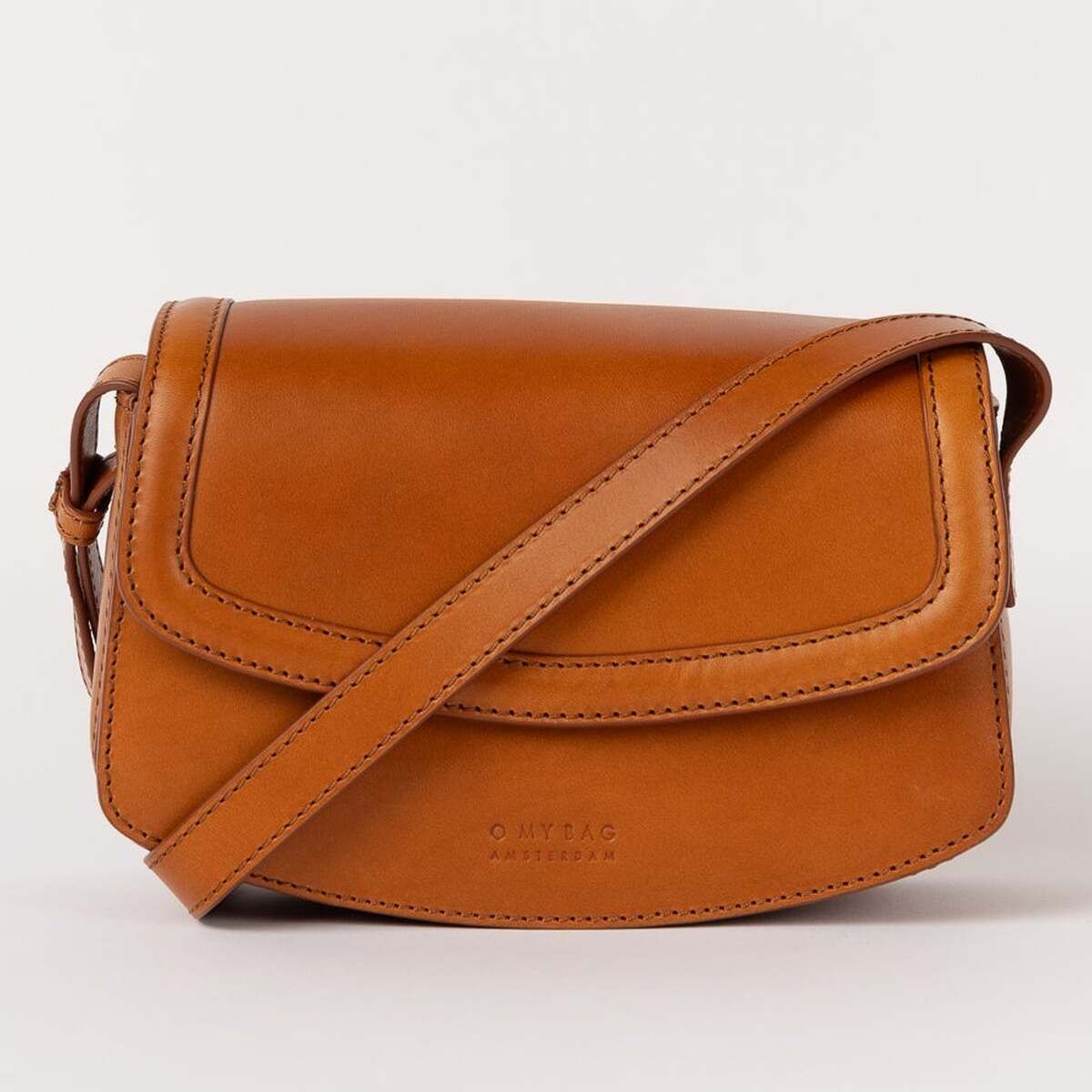 Eine kleine Umhängetasche in warmem Braunton aus glattem Material mit Überschlagklappe und längenverstellbarem Schulterriemen, vor hellem Hintergrund dargestellt.
