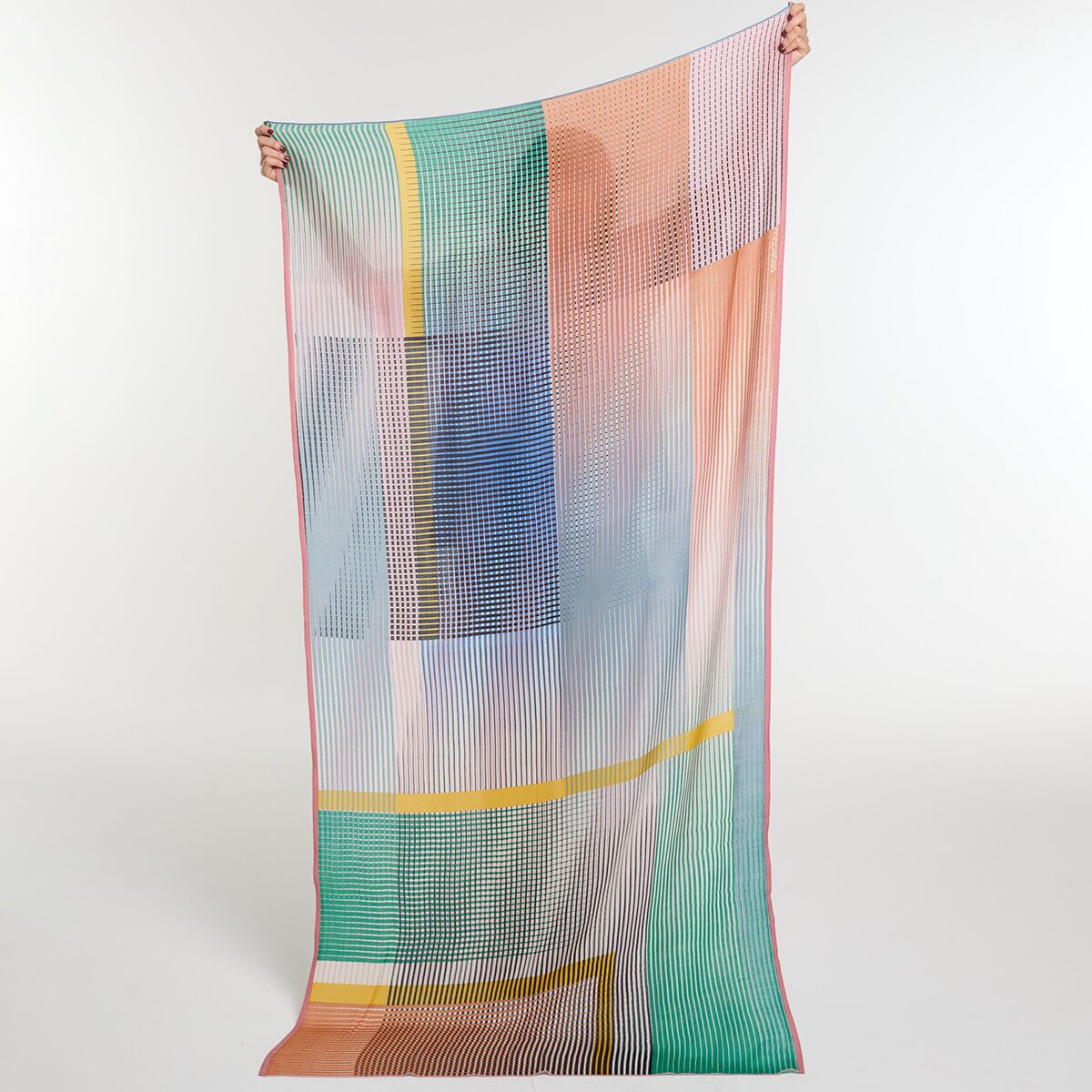 Ein großer, leichter Wollschal mit einem modernen, farbenfrohen Muster in Pastelltönen wie Rosa, Blau, Gelb, Grün und Orange. Der Schal wird an den Enden von einer Person gehalten und zeigt ein abstraktes Streifendesign. Das Foto präsentiert das Accessoire vor neutralem Hintergrund und hebt die Vielseitigkeit und die modische Ausstrahlung hervor.