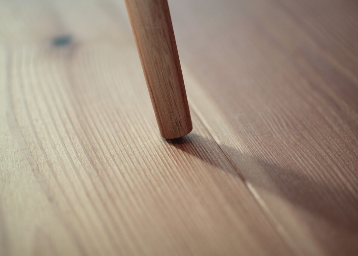Nahaufnahme eines hölzernen Beins eines Holzschemels »Heidi« auf einem Holzboden. Die Textur und Maserung des Holzes sind deutlich sichtbar.