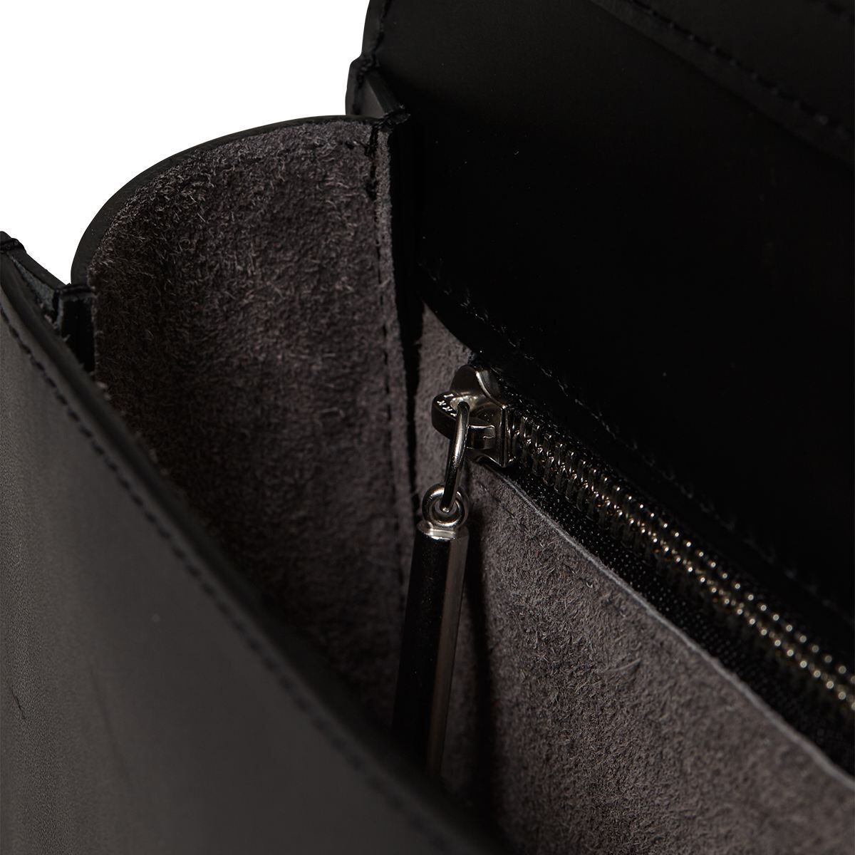 Eine elegante schwarze Schultertasche aus Leder, die Teil der ZEIT-Sonderedition ist. Sie verfügt über einen Reißverschluss und eine strukturierte Innenseite in grauem Stoff.