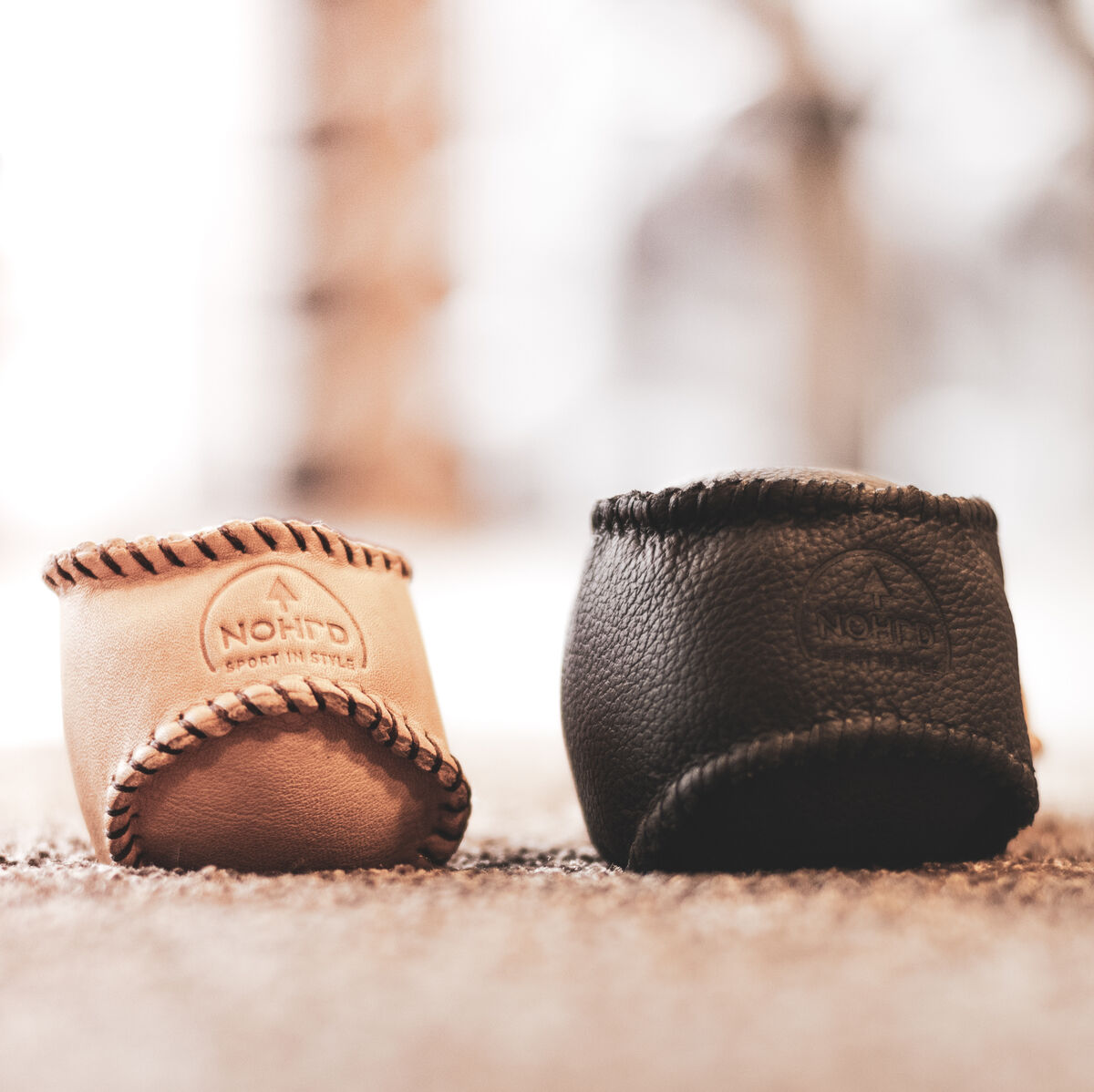 Zwei HaptikBälles auf einem strukturierten Teppich, ein Ball in Schwarz und der andere in Beige. HaptikBälles sind kleine, handgehaltene Trainingsgeräte, um Motorik und Handkraft zu verbessern.