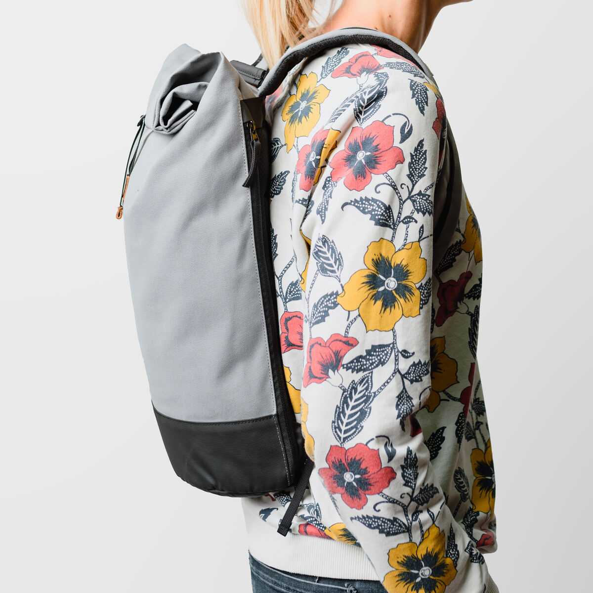 Person mit gemustertem Sweatshirt trägt einen grauen und schwarzen Rucksack der Marke Wanaka auf dem Rücken.