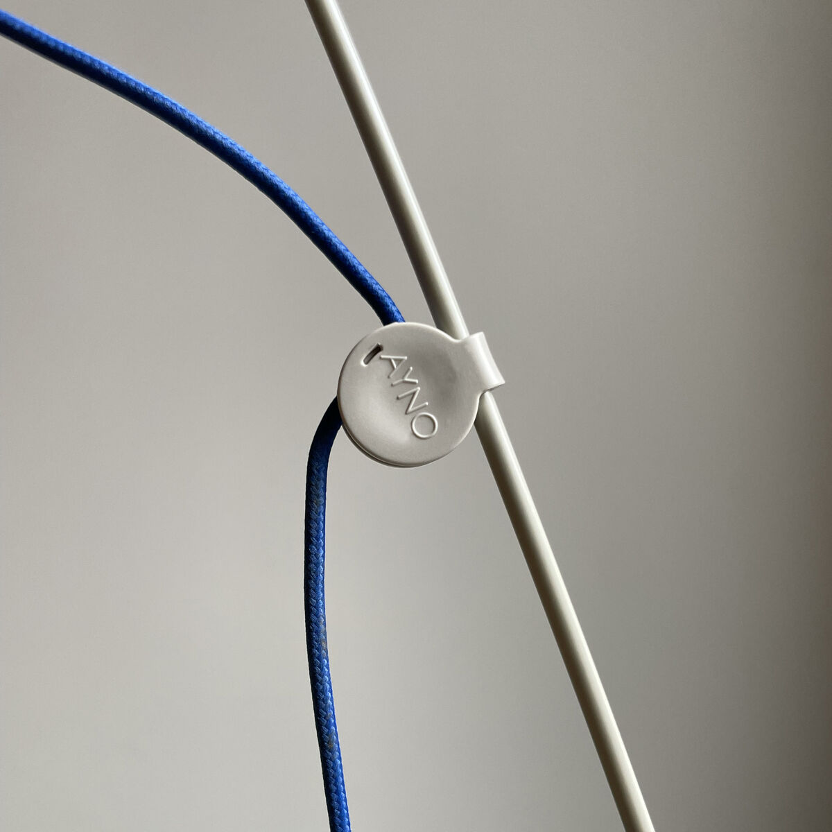 Detailaufnahme einer modernen Stehlampe der ZEIT-Sonderedition AYNO mit einem blauen Stromkabel aus Seide und einem silbergrauen Verbindungselement vor neutralem Hintergrund.