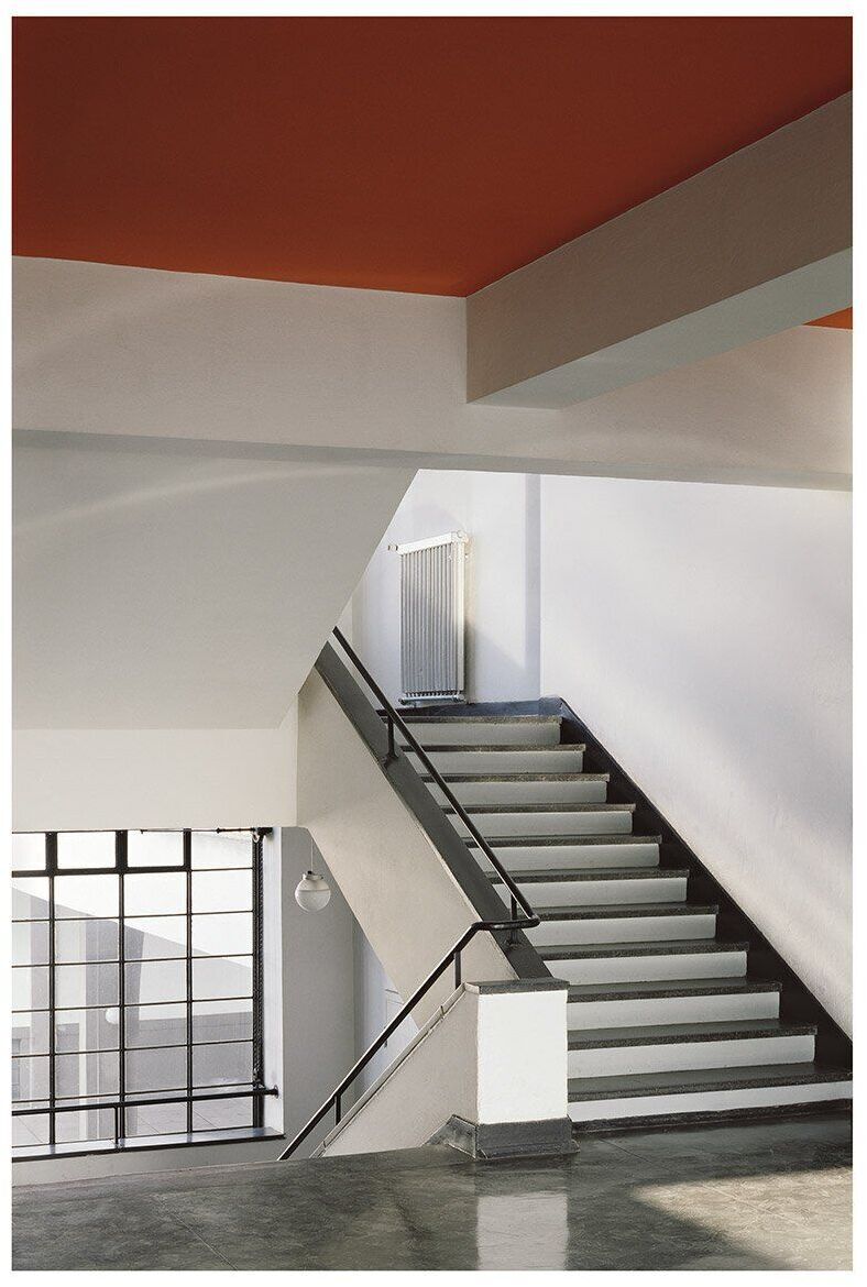 Fotografie von Klaus Kinold zeigt das Haupttreppenhaus im Bauhaus Dessau von Walter Gropius im Jahr 1992. Moderne Architektur mit klaren Linien und minimalistischen Design, weißen Wänden, einer grauen Treppe und einem orangefarbenen Deckenelement.