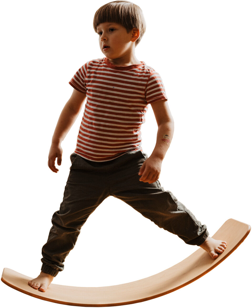 Ein Kind, das auf einem geölten Holz-Balance-Board steht und balanciert. Das Kind trägt ein rot-weiß gestreiftes T-Shirt und graue Hosen. Das Balance-Board ist leicht gebogen und aus hellem Holz gefertigt.