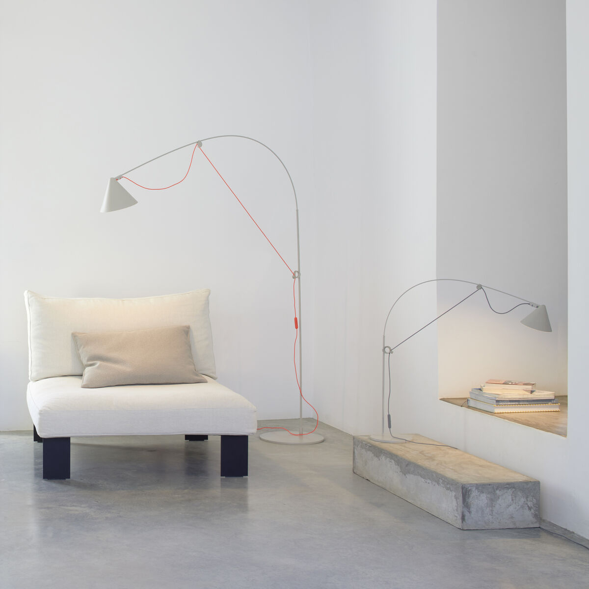 Eine moderne Stehlampe »AYNO« Silk in einem minimalistischen Wohnzimmer. Die Lampe hat ein orangefarbenes Kabel und Metallelemente, und sie steht neben einem weißen Sofa.