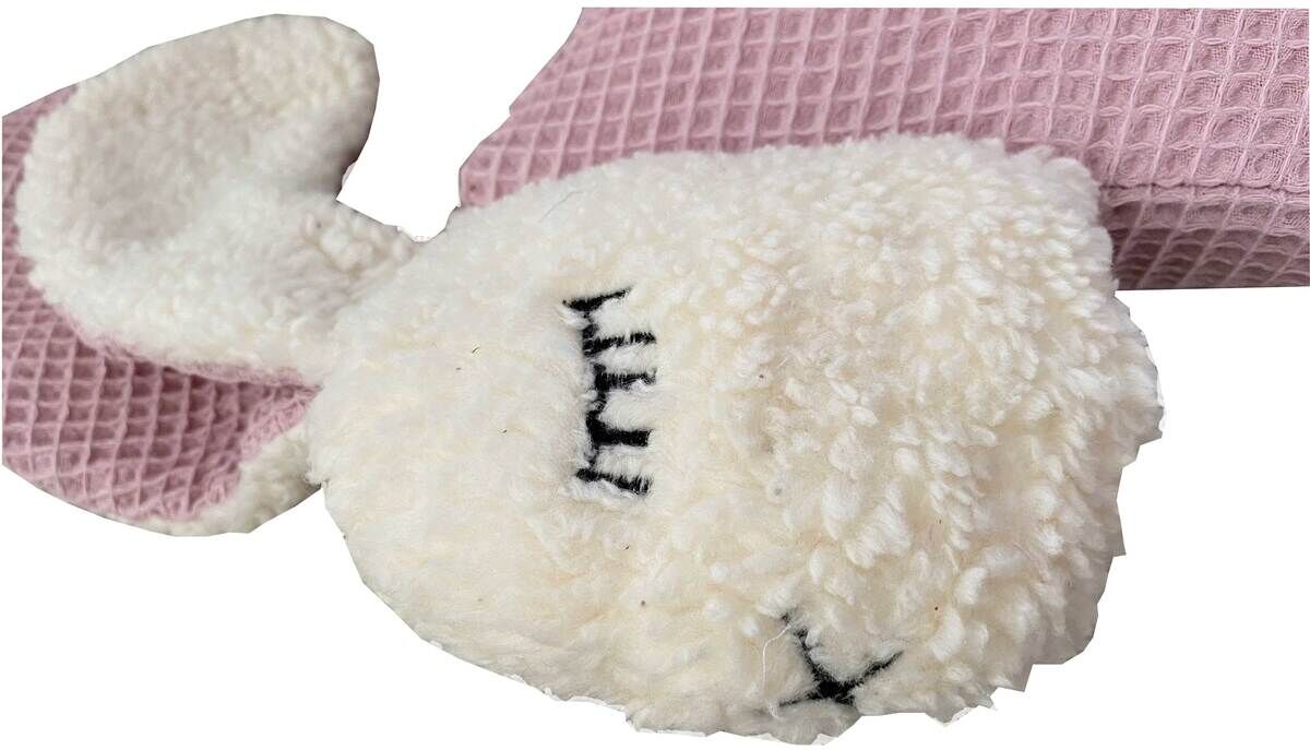 Kuscheltierkissen in Form eines Hasen mit weißen, flauschigen Stoff und geschlossenen Augen auf einer rosa strukturierten Decke.