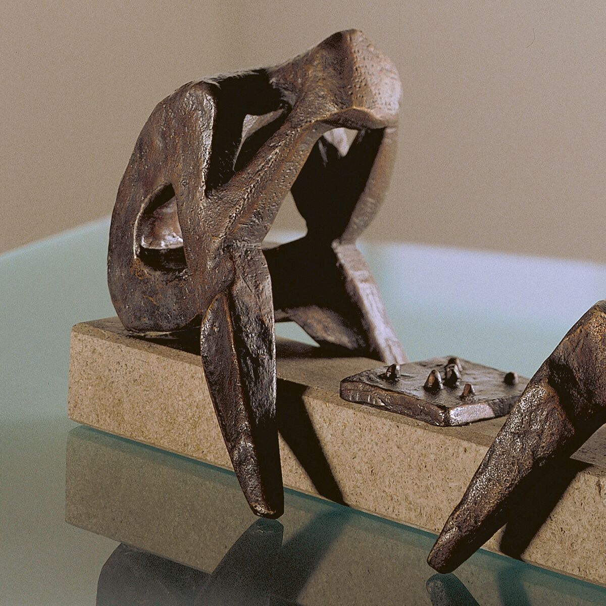 Detailreiche Bronzeskulptur von Sepp Mastaller: Zwei abstrahierte Figuren sitzen an einem rechteckigen Steintisch mit Schachbrett, ausgeführt im Wachsausschmelzverfahren. Oberfläche matt glänzend, feine Konturen. Die Skulptur steht auf einem massiven Sockel aus hellem Stein.