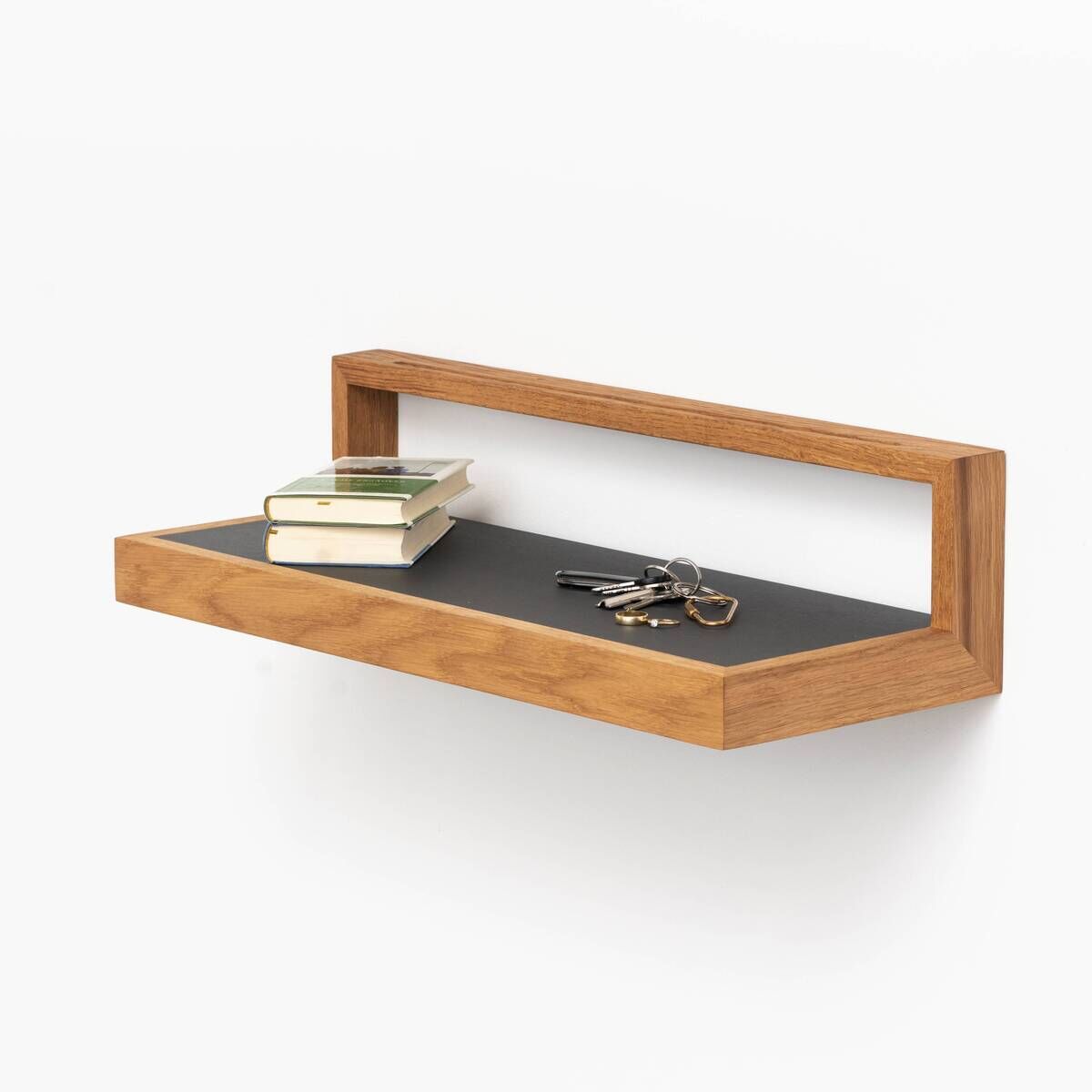 Ablagebord 'buck' in Anthrazit, montiert an einer weißen Wand und aus Holz, mit Büchern und Schlüsseln darauf.