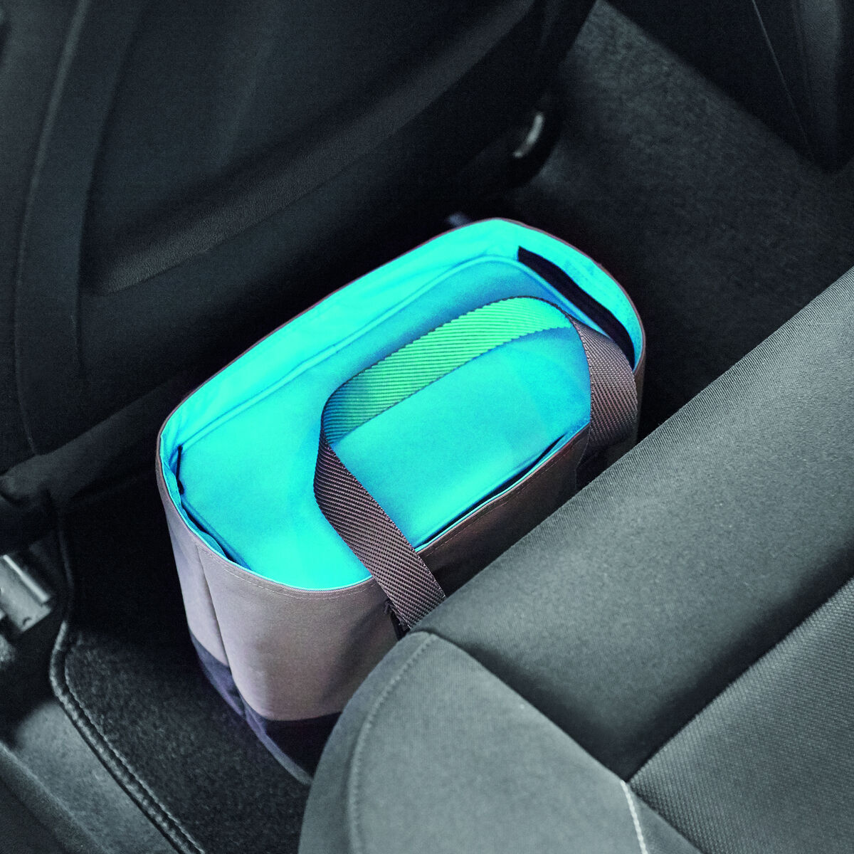 Bild einer Lunch-Tasche in Türkis und Blau, platziert im Fußraum eines Autos zwischen schwarzen Sitzen.
