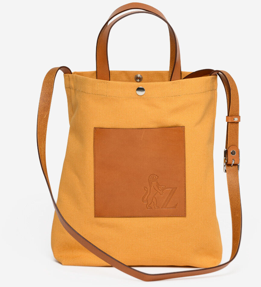 Eine stilvolle Einkaufstasche namens ZEIT Shop Jubiläums-Shopper aus orangefarbenem Stoff mit braunen Lederdetails. Ausgestattet mit Tragegriffen und einem verstellbaren Schultergurt.