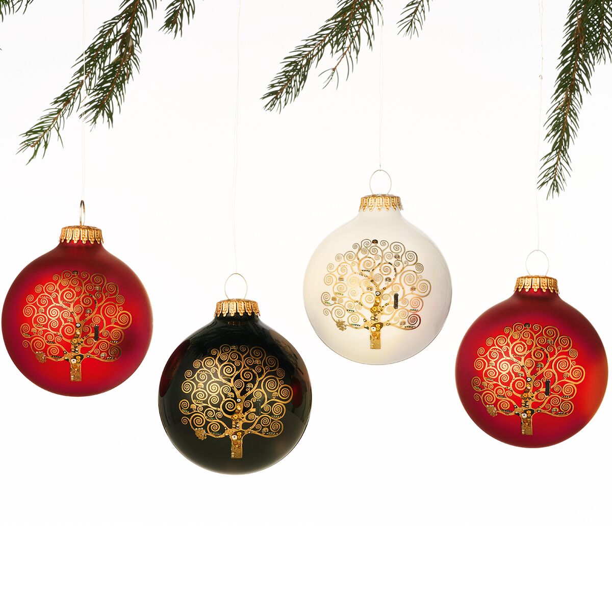 Vier edle Weihnachtsbaumkugeln aus Glas im Set mit dem Lebensbaum-Motiv nach Gustav Klimt, drei davon in Rot und eine in Weiß, jeweils mit goldener Verzierung. Die Kugeln hängen an goldenen Aufhängern und sind vor weißem Hintergrund mit einigen grünen Tannenzweigen dekorativ arrangiert.