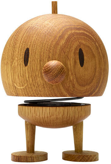 Eine Hoptimist Bumble-Figur aus Eichenholz mit einem fröhlichen Gesichtsausdruck und einer Metallfeder zwischen dem Kopf und dem Unterkörper. Die Holzfigur hat eine runde Form und steht auf zwei kleinen Beinen.