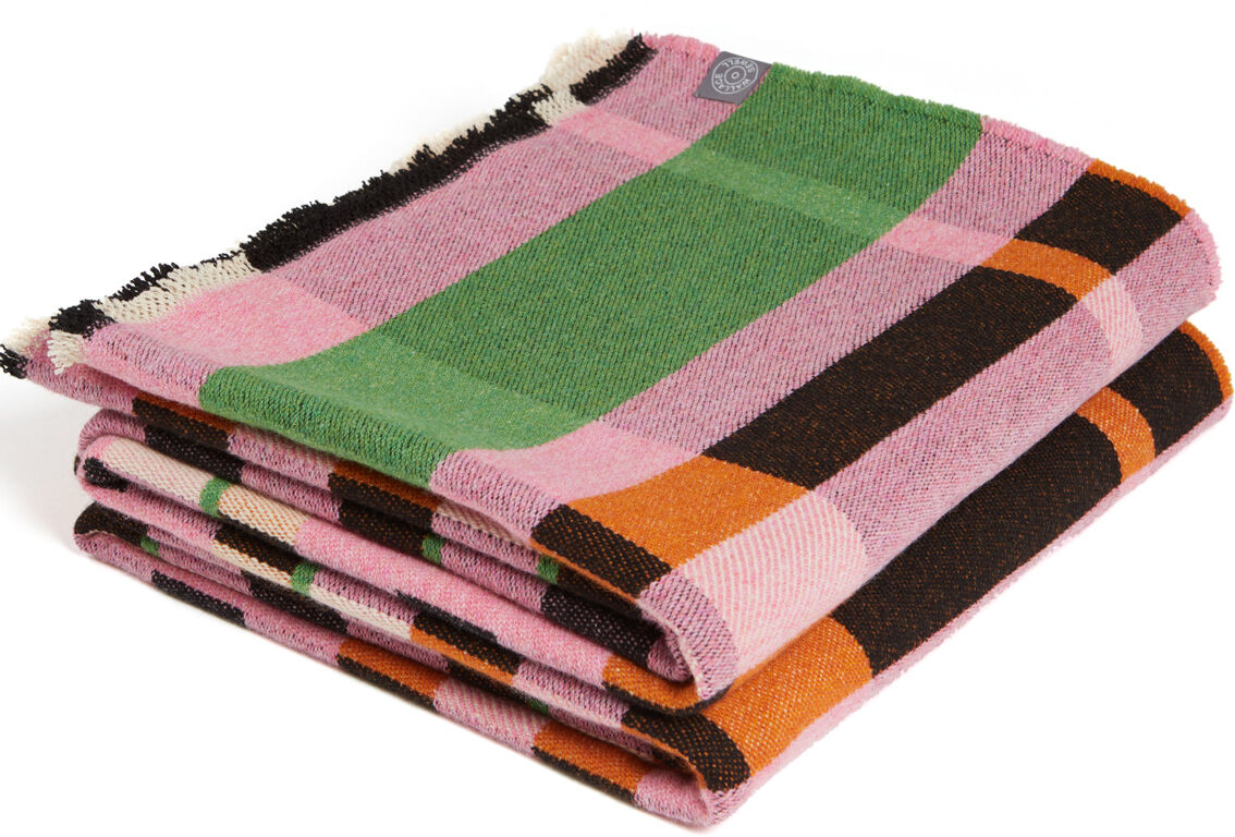 Eine Bauhaus Stölzl Decke L, die aus Wolle gefertigt ist, gefaltet und mit einem farbenfrohen Muster in Rosa, Grün, Orange, Schwarz und Weiß gestaltet.