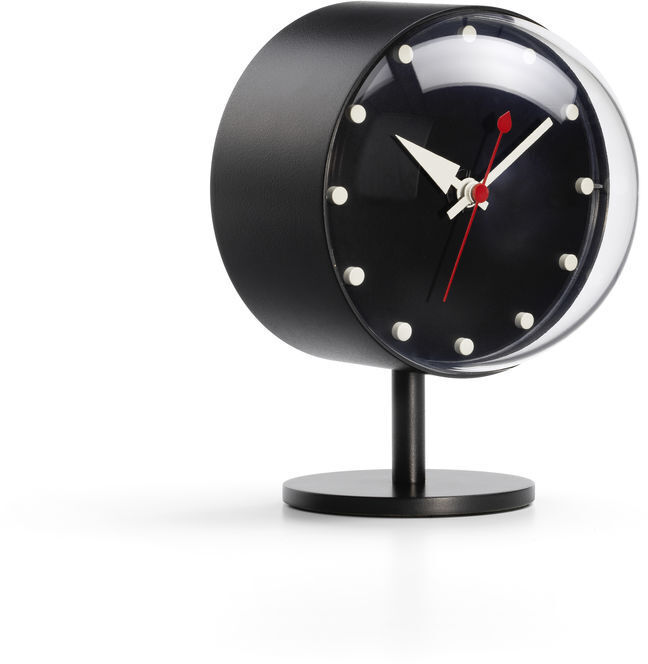 Tischuhr »Night Clock« mit einem runden schwarzen Gehäuse, weißen Zifferblatt-Markierungen und roten Zeigern, auf einem minimalistischen Standfuß platziert.