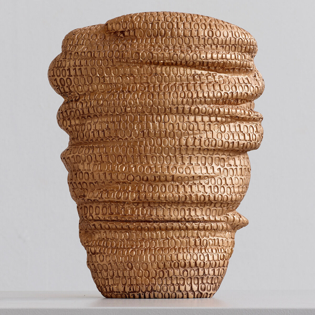 Goldene Skulptur mit ihrem einzigartigen Design und Zahlenmuster, die auf einem hellen Sockel platziert ist.