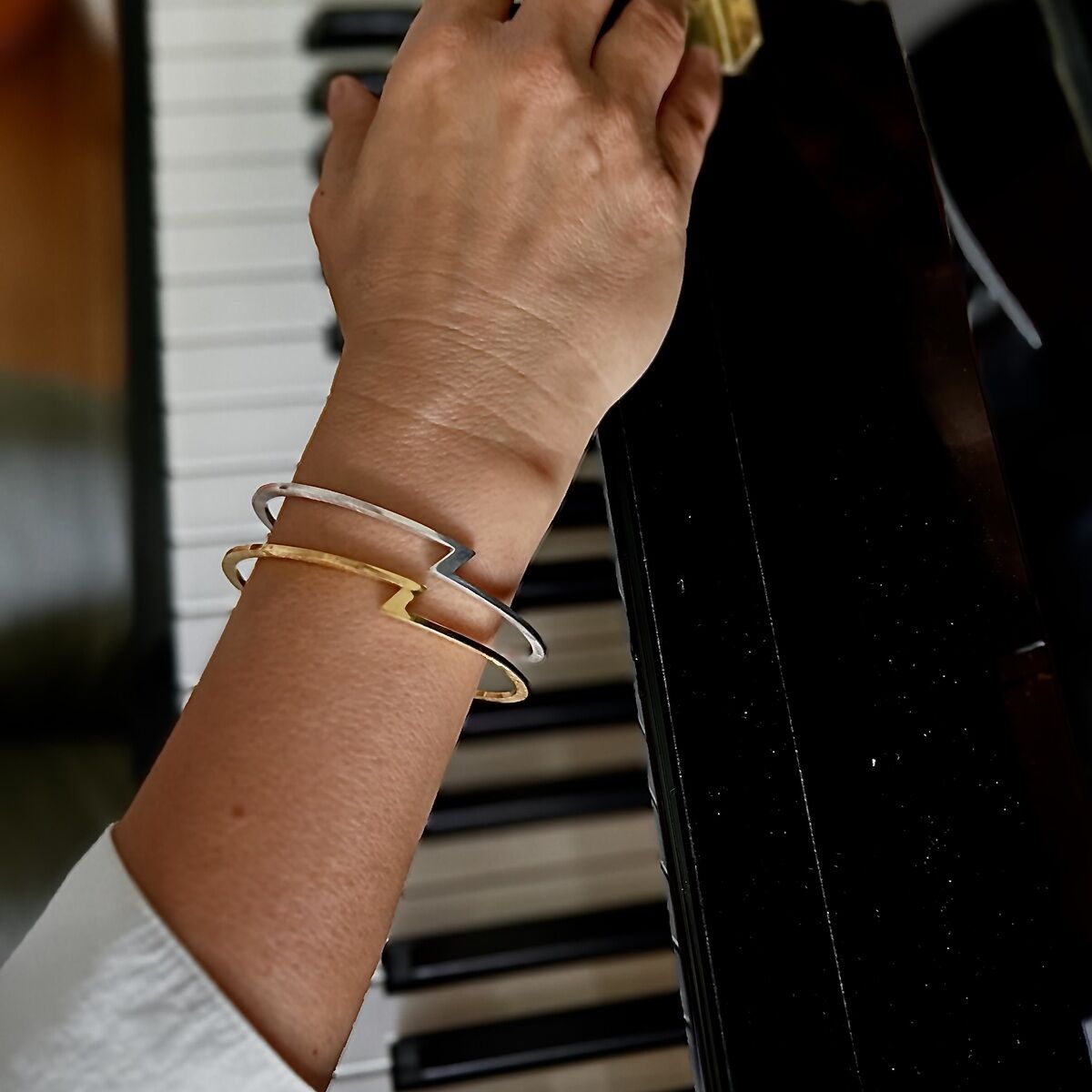 Eine Person spielt Klavier und trägt zwei Armreife der ZEIT-Sonderedition von HML Berlin, einen aus Silber und einen vergoldeten. Die Armreife zeigen das markante Z-Design und wirken elegant und zeitlos auf dem Klavierhintergrund.