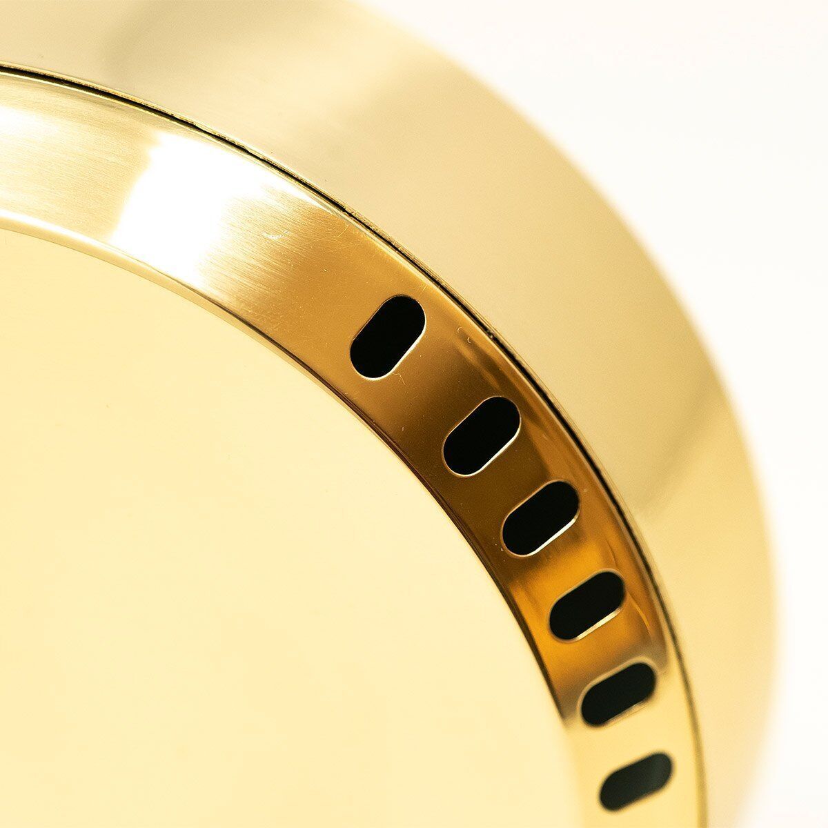 Nahaufnahme des ZEIT-Sonderedition“ POLAR Thermometer”. Das Bild zeigt einen Teil des runden Gehäuses aus glänzendem goldfarbenem Metall. Kleine schwarze Schlitze sind entlang des Randes sichtbar. Hintergrundelemente sind unscharf und minimalistisch.