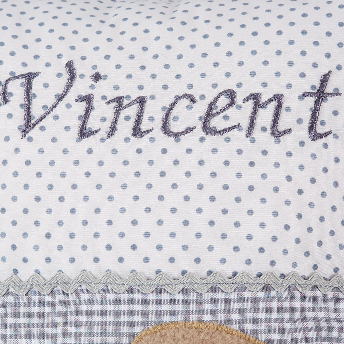 Ein weißes Kissen mit grauen Punkten und dem Namen 'Vincent' bestickt. Das Kissen hat ein Design mit einem blauen Stoffstreifen im Vichy-Karo-Muster und einem dekorativen Zickzackband. Ideal geeignet als personalisiertes Geschenk für Neugeborene.
