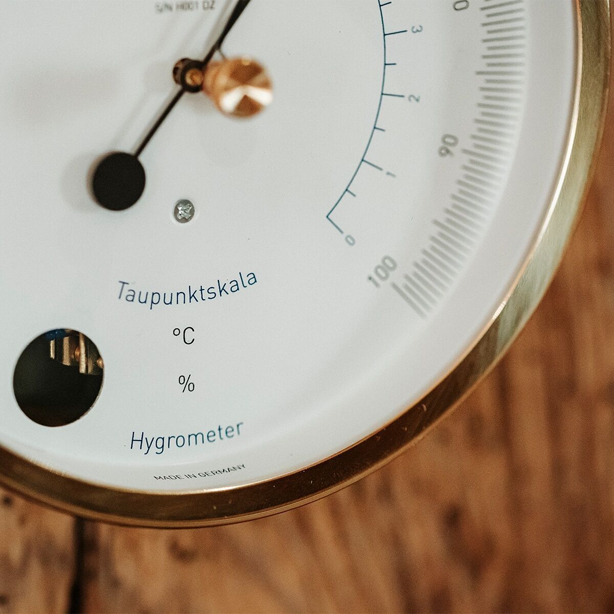 Detailaufnahme eines Haar-Hygrometers der ZEIT-Sonderedition »POLAR« mit einer Skala zur Anzeige der Luftfeuchtigkeit in Prozent und einer Taupunktskala in Grad Celsius. Das Gerät befindet sich in einem goldfarbenen Metallrahmen und steht auf einer Holzoberfläche.