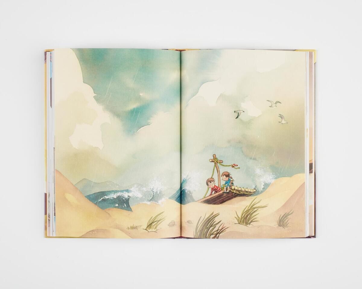 Ein aufgeschlagenes Kinderbuch zeigt eine Illustration eines Strandes mit einem kleinen Schiff. Zwei Figuren sind neben dem Schiff zu sehen, und Möwen fliegen am Himmel. Die Farben sind überwiegend blau, beige, braun, weiß und grün.